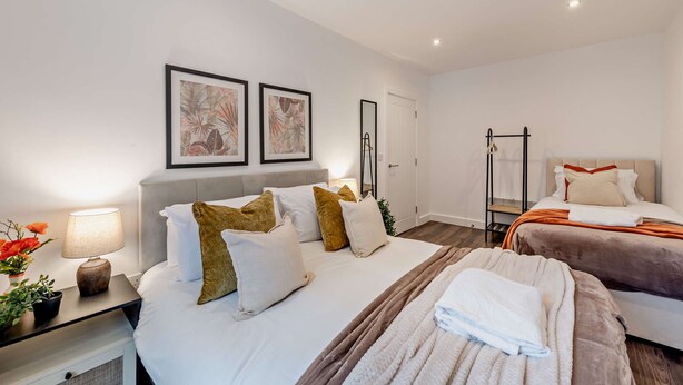 Quarto de hotel moderno com uma cama grande, uma mesa de cabeceira com abajur e duas molduras na parede.