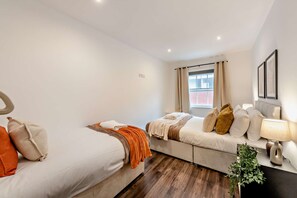 Ein Hotelzimmer mit zwei Betten, einem Sofa, einem Nachttisch mit Lampe und einem Vorhangfenster.