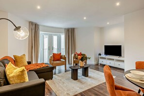 Ein modernes Wohnzimmer mit einer Couch, einem Sessel, einem Couchtisch und einem Fernseher.