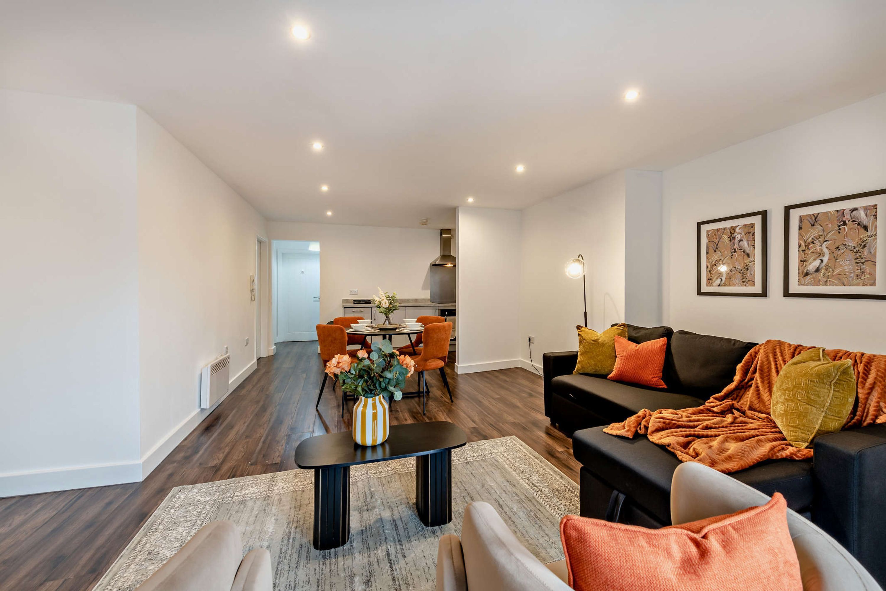 Ein modernes Wohnzimmer mit einer schwarzen Couch, orangefarbenen Kissen, einem Couchtisch und einem Essbereich mit orangefarbenen Stühlen.