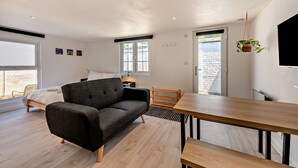 A modern bedroom with a bed, a sofa, a dining table, and a TV. - Host Stay - Studio 58 (Brighton)