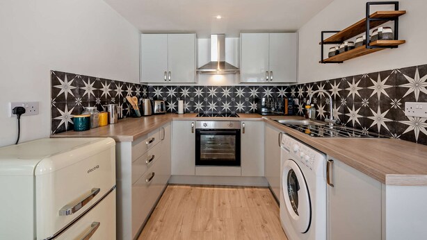 A compact kitchen with white cabinets, a built-in oven, a washing machine, and a microwave. - Host Stay - Studio 58 (Brighton)