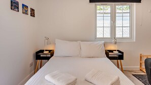 A bedroom with a bed, two bedside tables with lamps, a window with a view, and three wall-mounted pictures. - Host Stay - Studio 58 (Brighton)