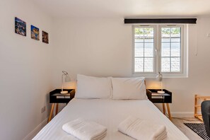 A bedroom with a bed, two bedside tables with lamps, a window with a view, and three wall-mounted pictures. - Host Stay - Studio 58 (Brighton)