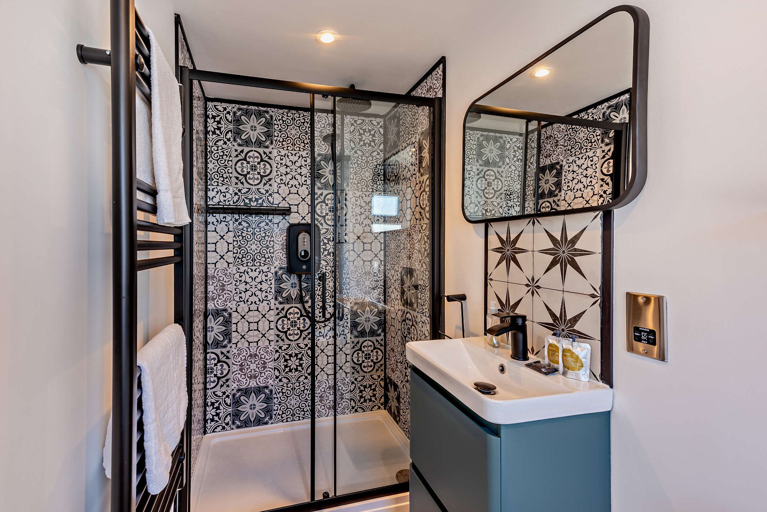 A bathroom with a glass-enclosed shower, a white sink, and a mirror with a geometric pattern.