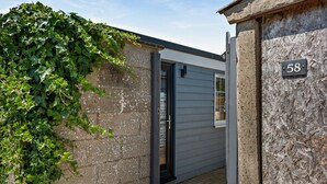 A narrow entrance with a concrete wall, a metal number plate, and a door leading to a room with a window. - Host Stay - Studio 58 (Brighton)