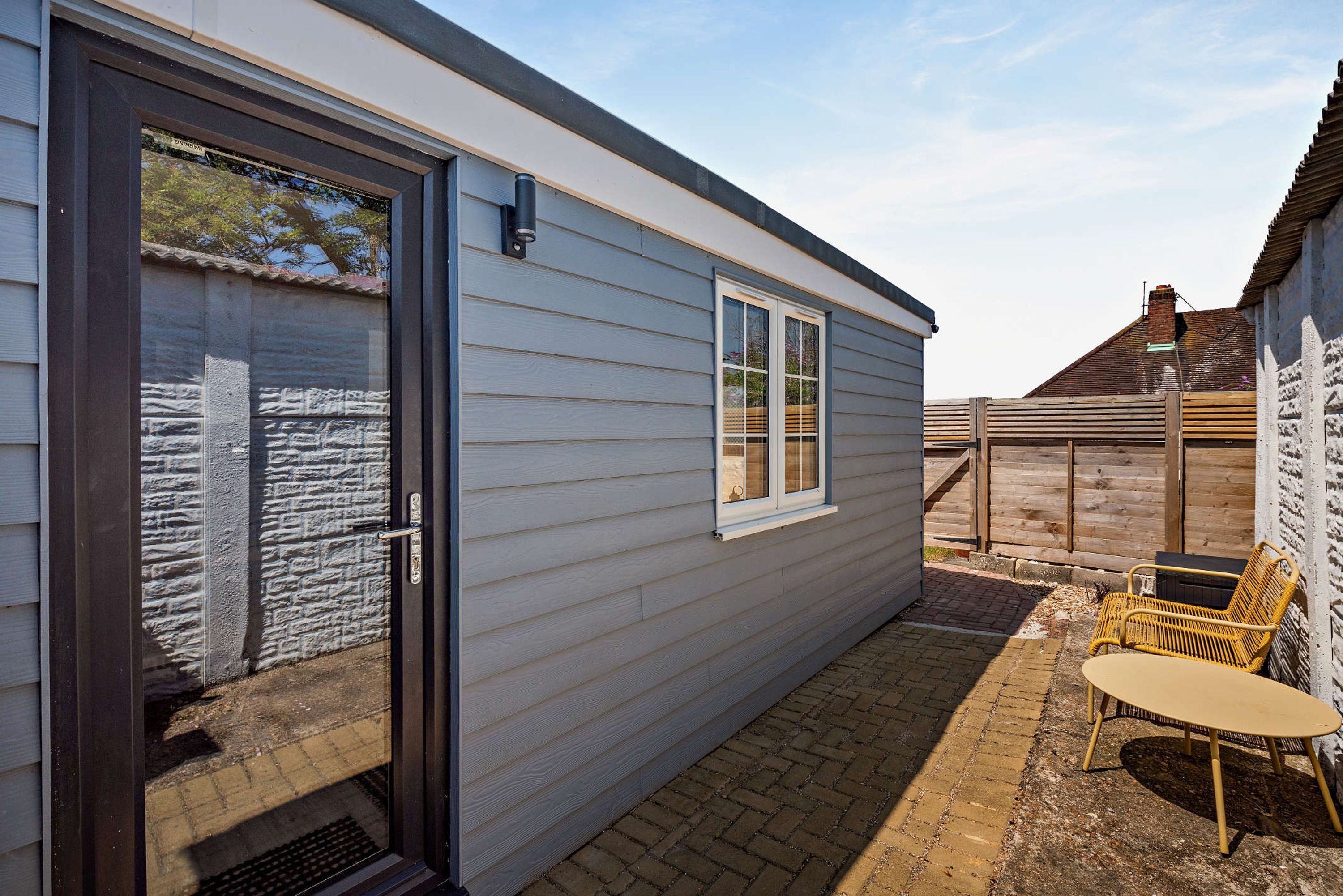 A single-story house with a sliding glass door, a small patio with a table and chairs, and a brick pathway leading to the door.