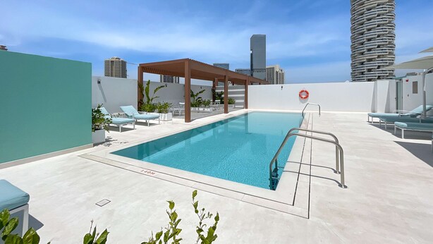 Ein Dachpool mit Liegestühlen und einer Pergola, umgeben von Stadtgebäuden.