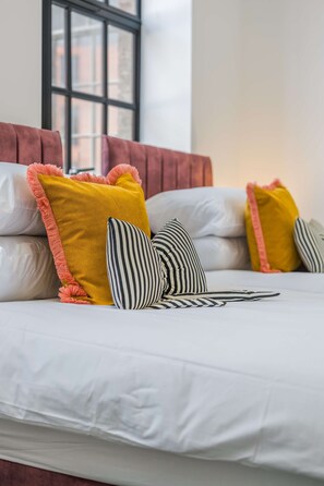 A bed with white bedding and multiple pillows, including a yellow one with a pink border and a striped one. - Stylish 2BR Apartment Jewellery Quarter 2 Ensuites Fast Wifi 8 Min to New St Station (Birmingham)