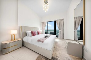 A hotel room with a large bed, a bedside table, a mirror, and a view of the city. - Free Housekeeping Visits During Your Stay - Stayshort - Modern 1BR in Prime Business Bay - 4 Guests (Dubai)