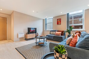 A modern living room with a flat-screen TV, a sofa, a coffee table, and a large window. - Hartley Hill Gem - Modern Apartment Near Leeds Centre (Leeds)