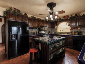 A kitchen with dark wooden cabinets, a black refrigerator, a stove, and a ceiling fan. - Authentic Beachfront Home | Panoramic Ocean Views (Puerto Peñasco)