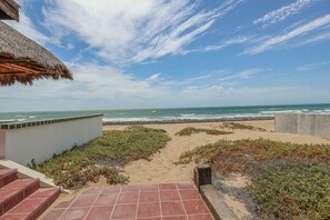 A beach view with a pathway leading to the sea, a thatched roof structure, and a concrete wall. - Authentic Beachfront Home | Panoramic Ocean Views (Puerto Peñasco)