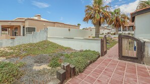 A gated residential area with a paved walkway, palm trees, and a clear sky. - Authentic Beachfront Home | Panoramic Ocean Views (Puerto Peñasco)