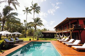 A pool area with lounge chairs and umbrellas, surrounded by palm trees and a building with a red facade.