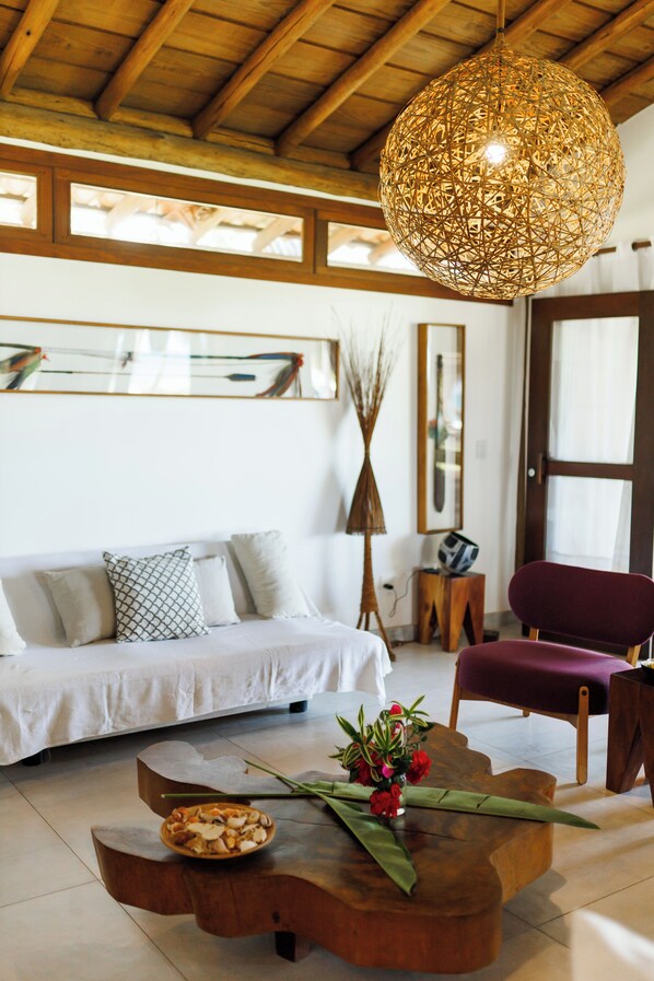 A modern living room with a wooden ceiling, a white sofa, a purple chair, a coffee table with a vase of flowers, and a hanging light fixture.