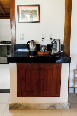 A kitchen with a black countertop, wooden cabinets, a kettle, a coffee maker, and a framed picture on the wall.