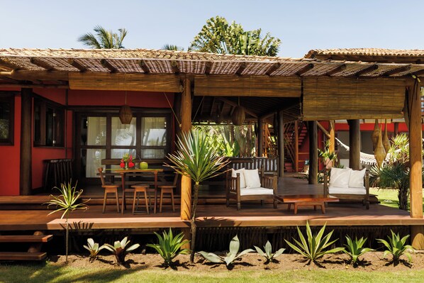 A covered outdoor seating area with wooden furniture and a red building in the background.