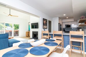 Ein modernes Wohnzimmer mit Kamin, eine Essecke mit blauen Unterlagen und eine Küche mit einem Edelstahlkühlschrank.