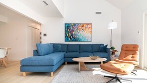 Een moderne woonkamer met een hoekbank, een ronde salontafel, een fauteuil en een kleurrijk abstract schilderij aan de muur.