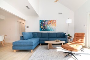 A modern living room with a sectional sofa, a round coffee table, a single arm chair, and a colorful abstract painting on the wall. - Family Retreat Near Beach | 2 Decks, Access To Pool & Tennis (Rehoboth Beach)