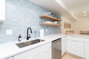 Eine moderne Küche mit blauen Fliesen an der Spritzschutzwand, weißen Schränken und einer Spüle aus Edelstahl.