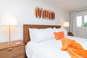 A hotel room with a wooden headboard, white bedding, an orange throw blanket, and a wall art piece. - Family Retreat Near Beach | 2 Decks, Access To Pool & Tennis (Rehoboth Beach)