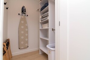 Un espace buanderie bien organisé, avec un fer à repasser, des étagères où sont pliés les vêtements et un panier.