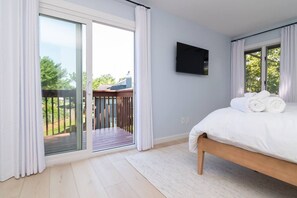 Ein Schlafzimmer mit Bett, einem an der Wand montierten Fernseher und einem Balkon mit Blick ins Freie.