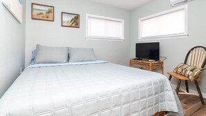 Un dormitorio con una cama, un televisor sobre una mesita de noche y dos ventanas.