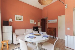 A dining area with a round table, chairs, and a sofa. There is a television on a stand, a lamp, and framed pictures on the wall. - Suoerb Apartment With Garden Heart of Deauville (Deauville)