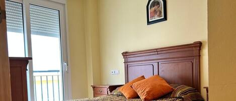 Un dormitorio con cama, mesita de noche, cabecera de madera, candelabro, ventana con persianas e imagen enmarcada en la pared.