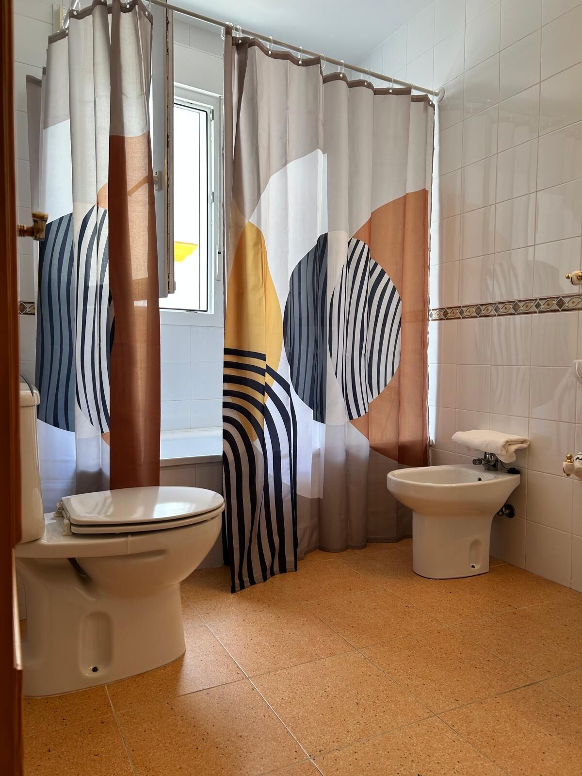 A bathroom with a toilet, bidet, and a shower curtain with abstract patterns.