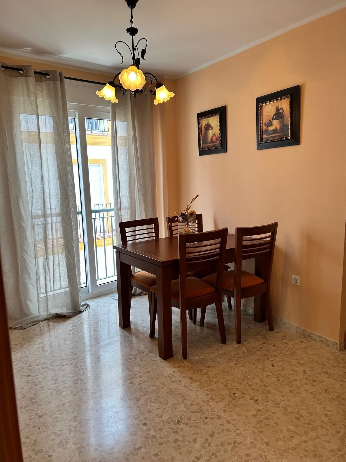 Uma sala de jantar com uma mesa e cadeiras, um candelabro e duas imagens emolduradas na parede.