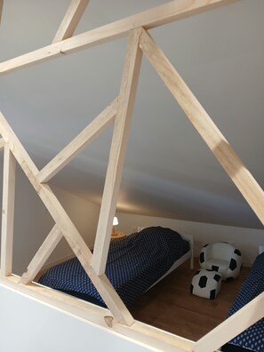 Ein Zimmer mit einer geometrischen Holzstruktur, einem Bett mit gemusterten Betttextilien und zwei ottomanartigen Hockern in Fußballform.