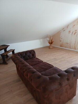 Ein Zimmer mit einem braunen, gesteppten Sofa, einer Holzbank und einer dekorativen Vase mit getrockneten Pflanzen.
