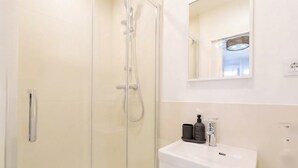 A modern bathroom with a glass shower enclosure, a white sink, and a mirror above the sink.