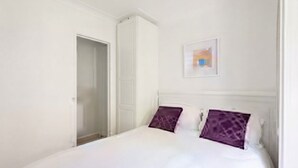 A bedroom with a bed, white walls, a door, and a framed picture on the wall.