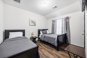 Ein Hotelzimmer mit zwei Einzelbetten, einem Nachttisch mit Lampe, einem kleinen Tisch und einem Fenster mit Vorhängen.