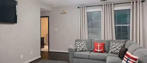 A living room with a grey sofa, ottoman, ceiling fan, and a flat-screen TV.