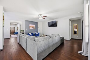 Ein modernes Wohnzimmer mit einem grauen Ecksofa, einem Deckenventilator und einem flachbildfernseher an der Wand.