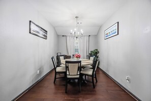 Een eetruimte met een ronde tafel, stoelen, een kroonluchter en lijstwerken aan de wanden.