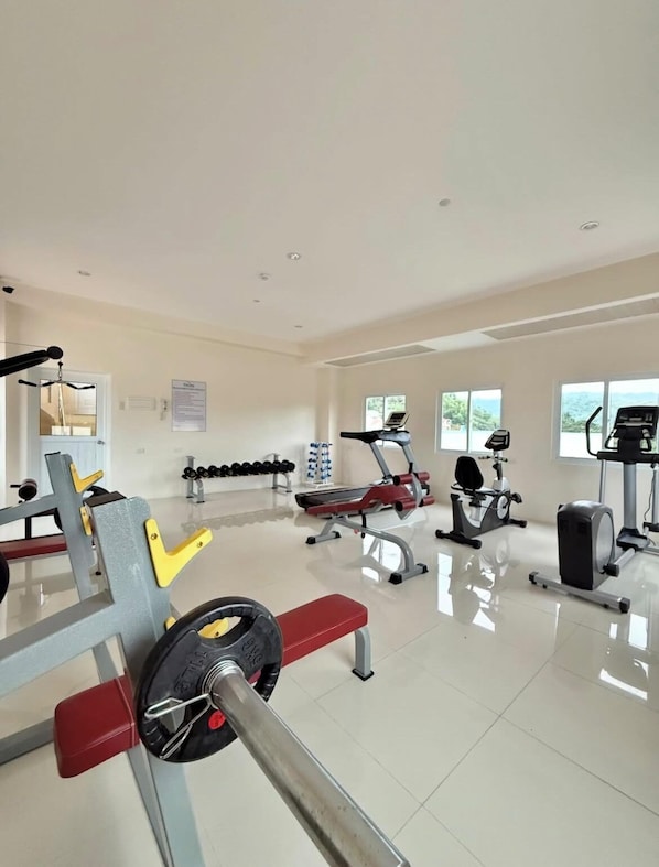 Un gimnasio con diversos equipos de ejercicio, incluyendo una prensa de banca, mancuernas y máquinas de cardio.