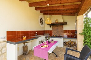 An outdoor kitchen with a brick fireplace, a table set for dining, and a hanging light fixture. - The <b>Villa Son Fornes</b> has 3 bedroom(s) and capacity for 6 people. (Buger)