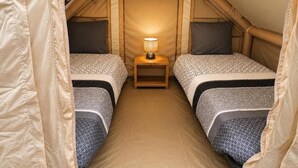 Een tentkamer met twee bedden, een nachtkastje met een lamp, en een uitzicht op het interieur van de tent.