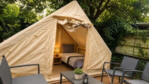 Een tent met een bed, een tafel en stoelen op een houten terras.