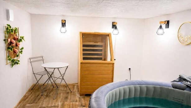 Een kamer met een houten vloer, een rond opblaasbaar bubbelbad, een klein tafeltje met een stoel en een houten deur met een raam.