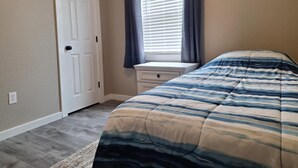 A bedroom with a bed, a window with curtains, a dresser, and a door.