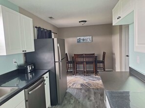 Una cocina compacta con refrigerador, estufa y tostadora. Hay un comedor con mesa y sillas.