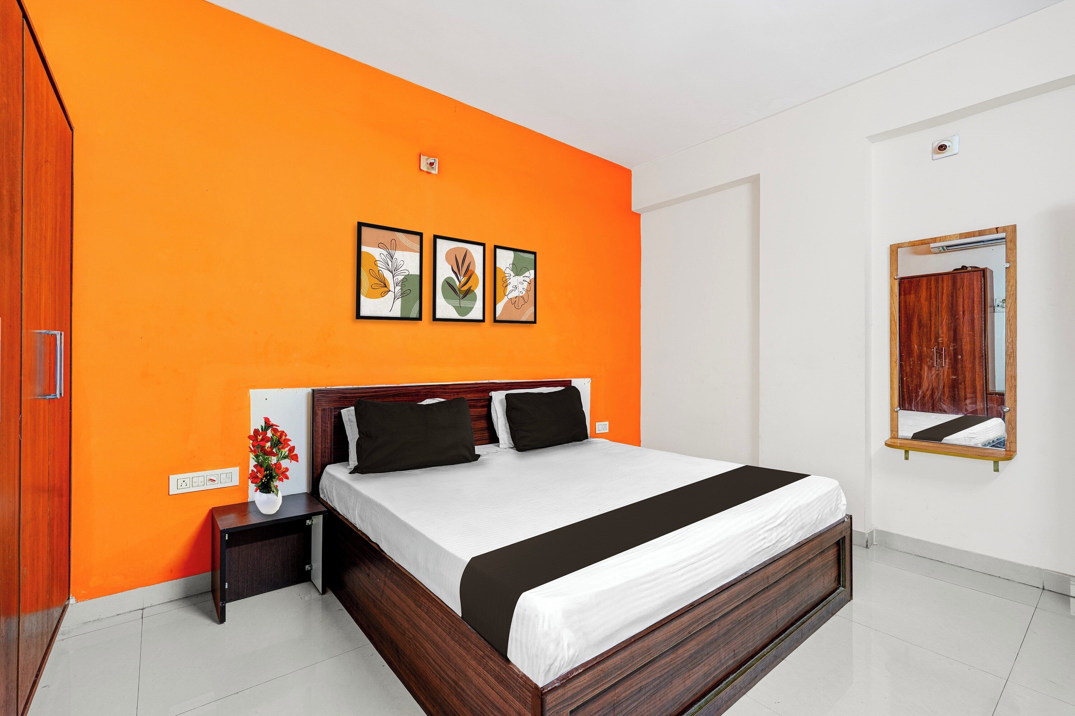 A bedroom with a large bed, a nightstand, a mirror, and three framed pictures on the wall.